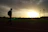 Close-up of a fan proudly wearing the élite t-shirt, standing against a backdrop of a running track at sunset.