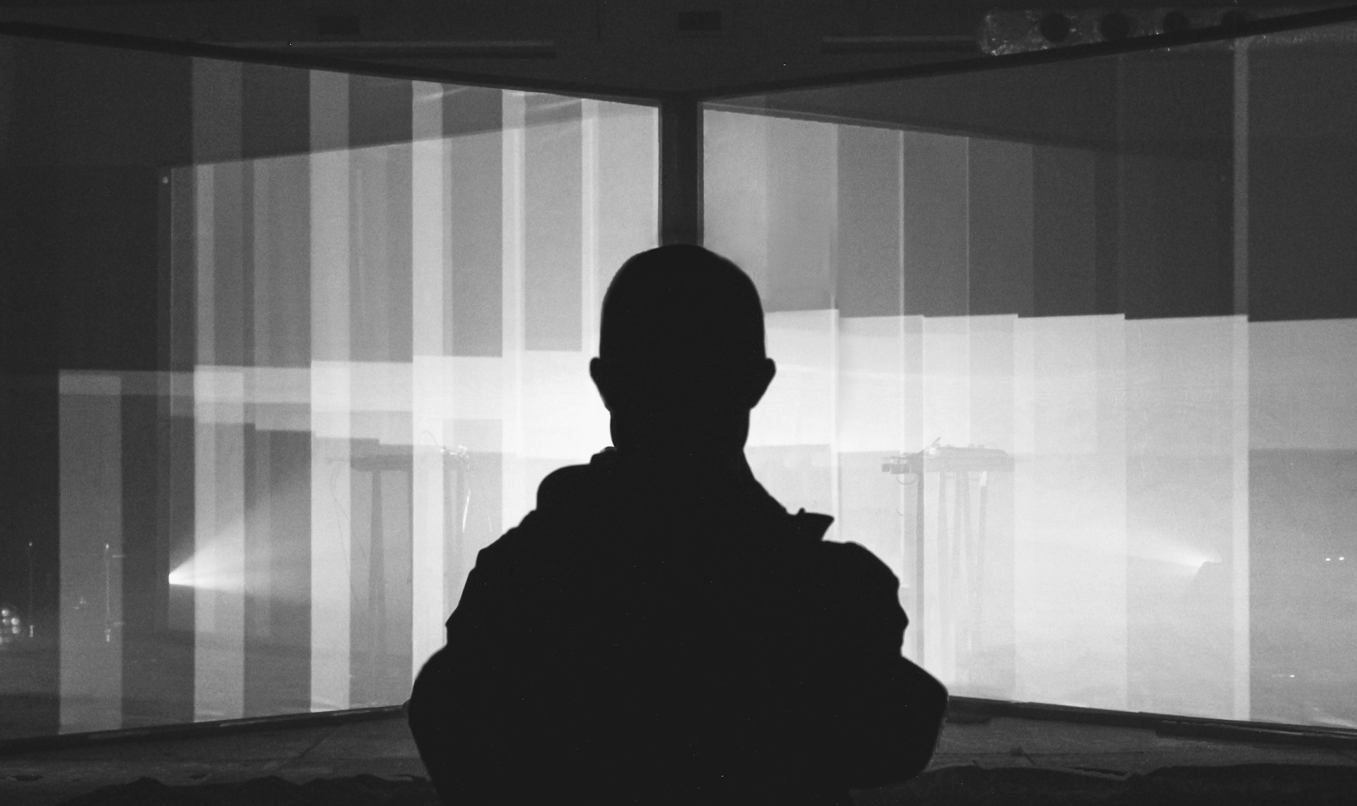 A person is standing in front of a large, illuminated backdrop with various vertical striped patterns. The scene is in black and white, with the person silhouetted against the bright background.