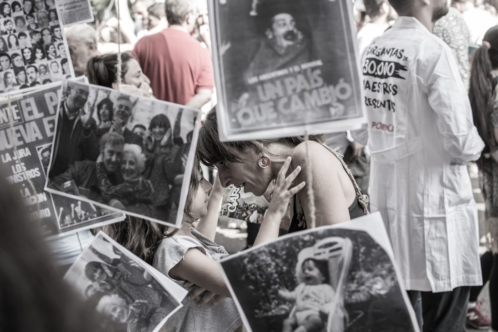 fotografia in scala di grigi di donna e ragazza faccia a faccia mentre copre foto assortite