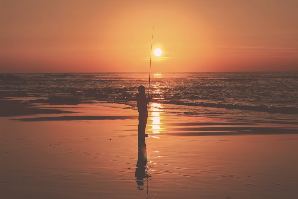 Fotografía de silueta de persona sosteniendo caña de pescar cerca del cuerpo de agua