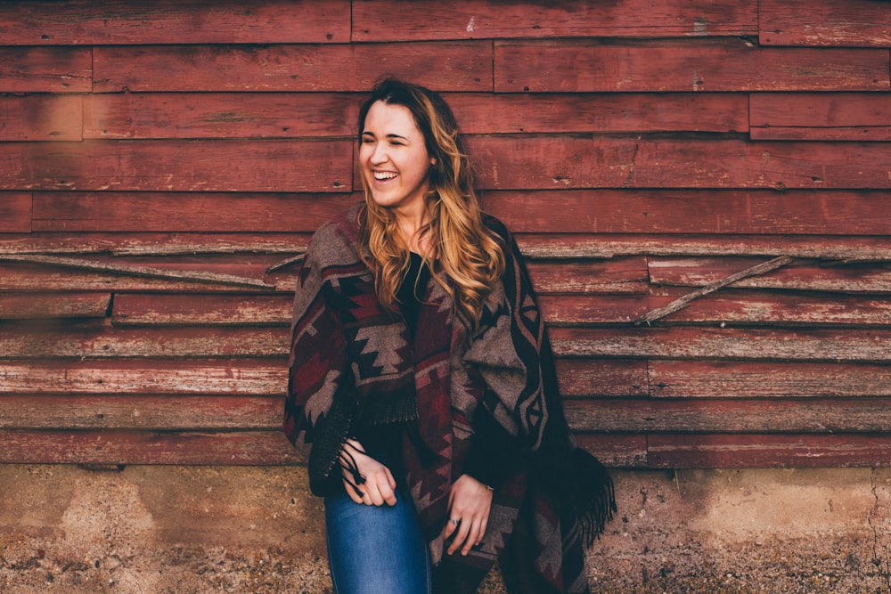smiling woman wearing brown and black poncho leaning on wall