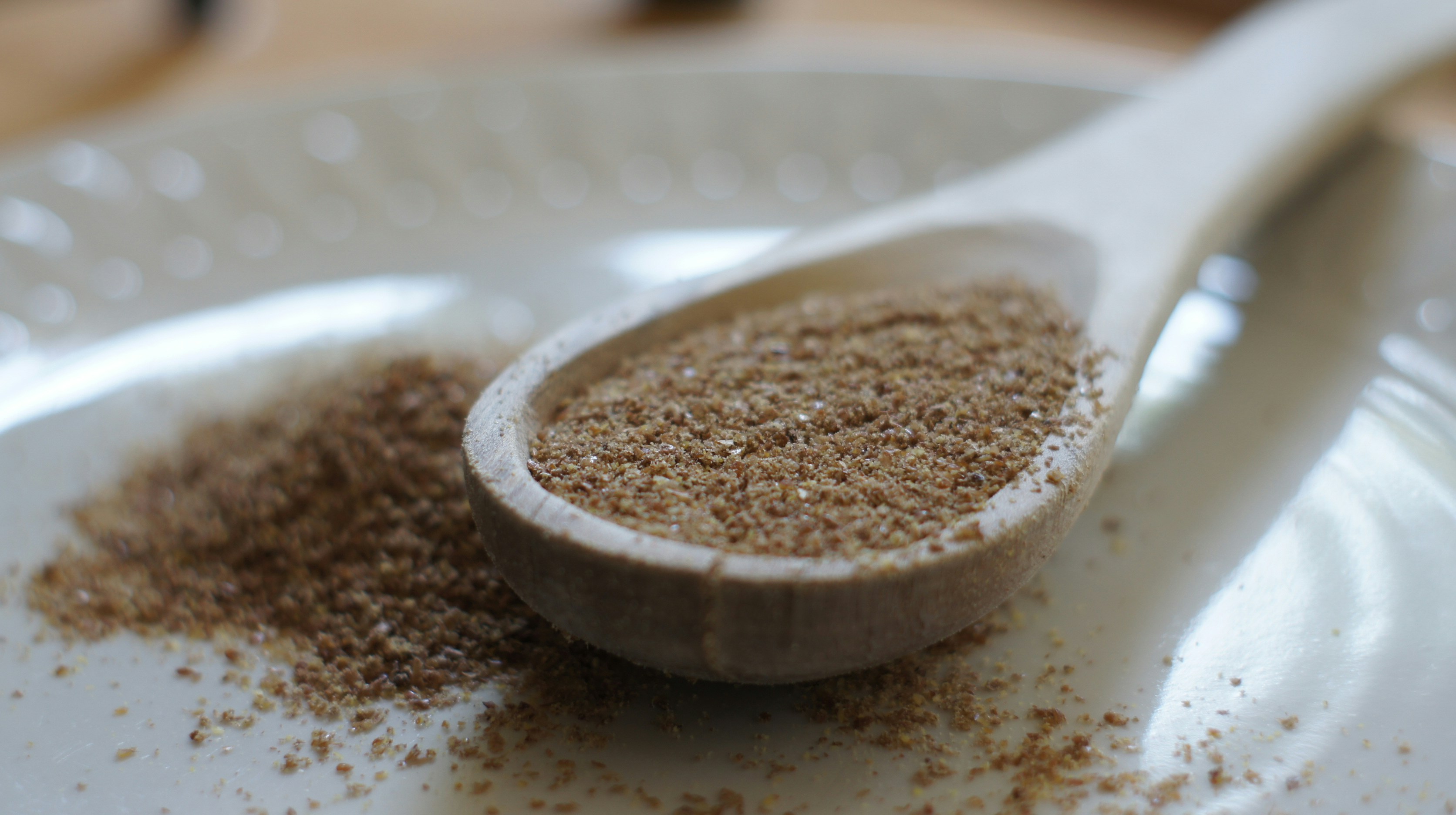 Brown flax seeds in a wooden spoon on a rustic surface, warm tones