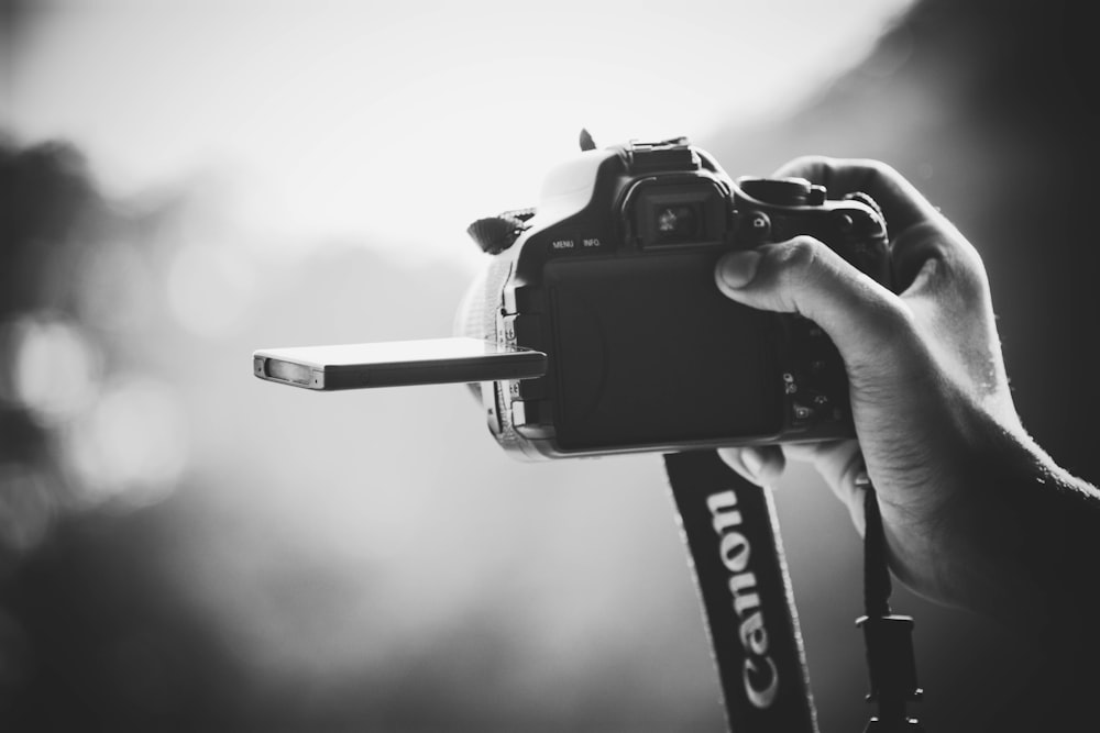 fotografia in scala di grigi di una persona che tiene in mano una fotocamera reflex digitale Canon