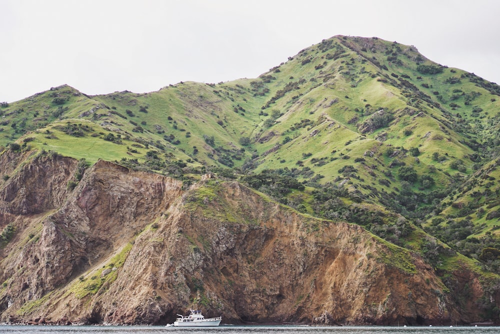 green mountain near body of water with white watercraft during daytime