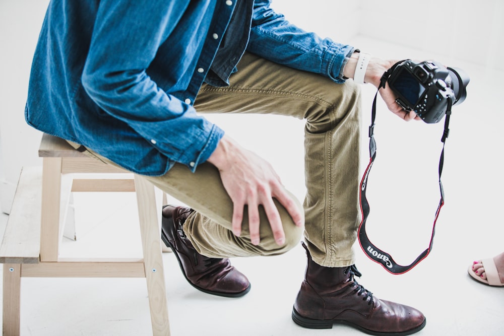 man holding DSLR camera while sitting on stool