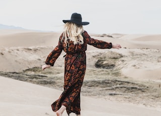 photo of person wearing brown and orange floral maxi dress walking barefooted along deserted land