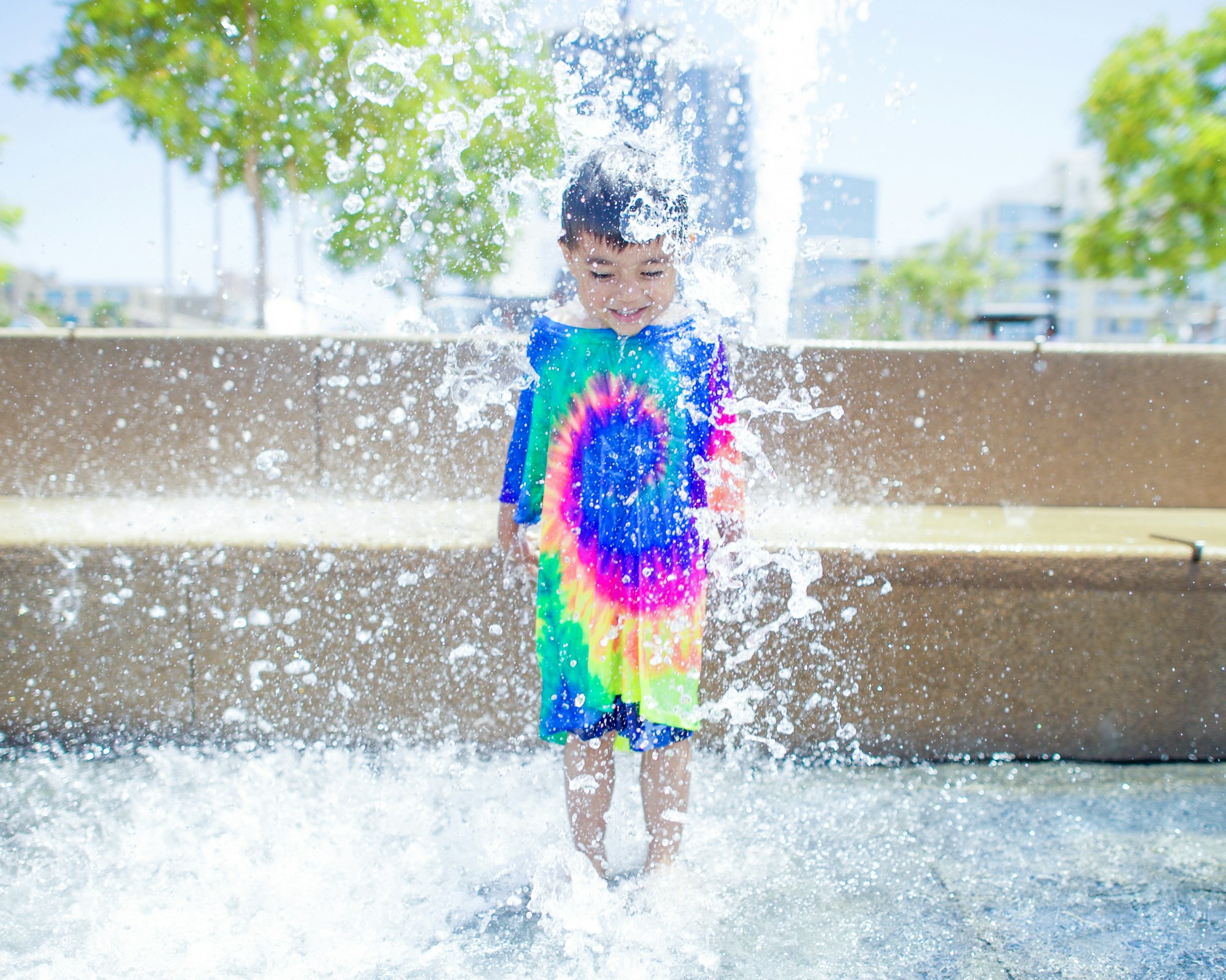 A child wearing a tie-dyed shirt while playing with water splashes.