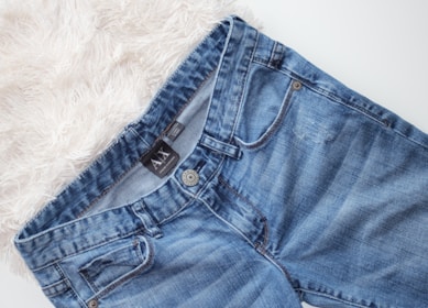 A pair of blue denim jeans with a visible brand tag on the waistband, placed on a white, fluffy surface.