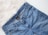 A pair of blue denim jeans with a visible brand tag on the waistband, placed on a white, fluffy surface.