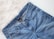 A pair of blue denim jeans with a visible brand tag on the waistband, placed on a white, fluffy surface.