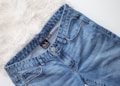 A pair of blue denim jeans with a visible brand tag on the waistband, placed on a white, fluffy surface.