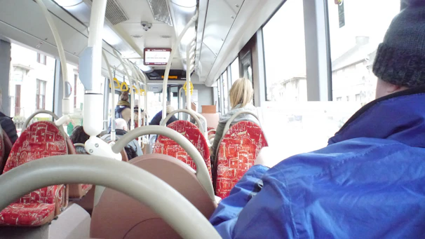 A modern red passenger bus parked at a clean, bright station with happy passengers boarding.