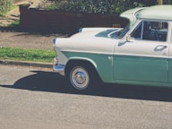 white and teal classic vehicle parking on road near brown railings beside green plants at daytime
