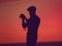 A silhouette of a person holding a camera against a vibrant sunset background. The scene is dominated by deep reds and oranges, creating a striking and dramatic backdrop. The figure appears to be focused on capturing the moment, highlighting a passion for photography.