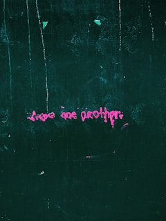 Pink graffiti text on a dark green textured wall, featuring abstract and slightly messy writing.