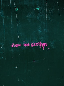 Pink graffiti text on a dark green textured wall, featuring abstract and slightly messy writing.