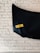 A black object is mounted on a white brick wall with a yellow sticker displaying the word 'DRUGS' in bold letters.