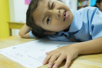 A focused student sitting at a desk surrounded by study materials, looking frustrated but determined.