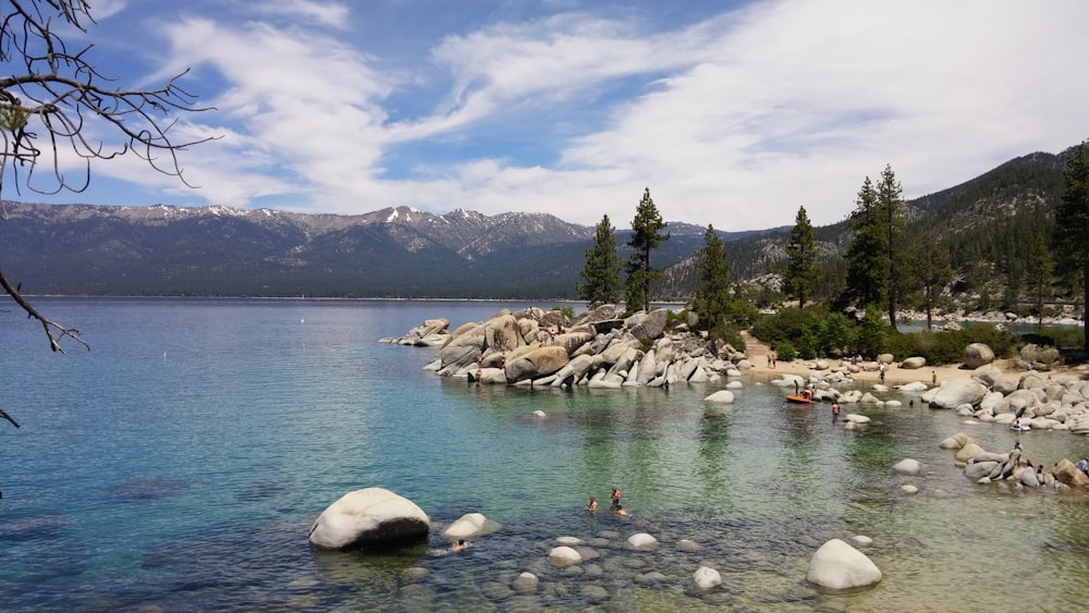 calm body of water surrounded with rocks and trees under blue sky