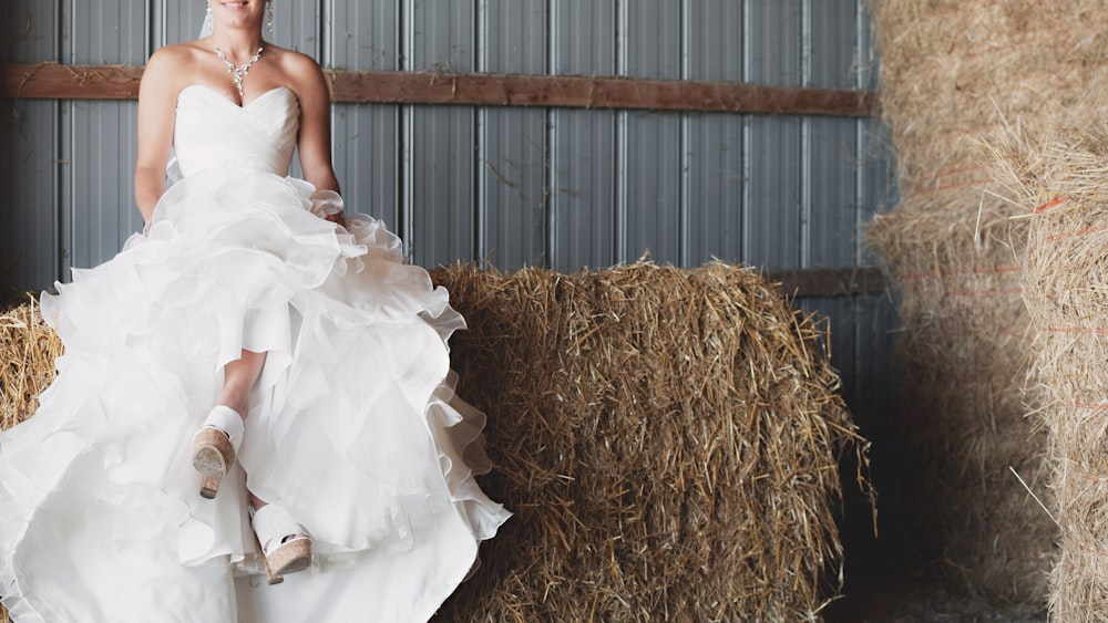 femme en robe de mariée à volants assise sur une botte de foin