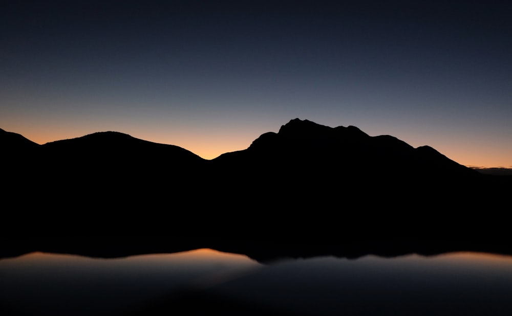 silhouette photography of mountain near body of water