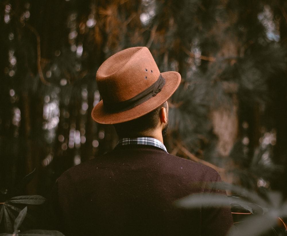 person wearing brown fedora hat facing trees