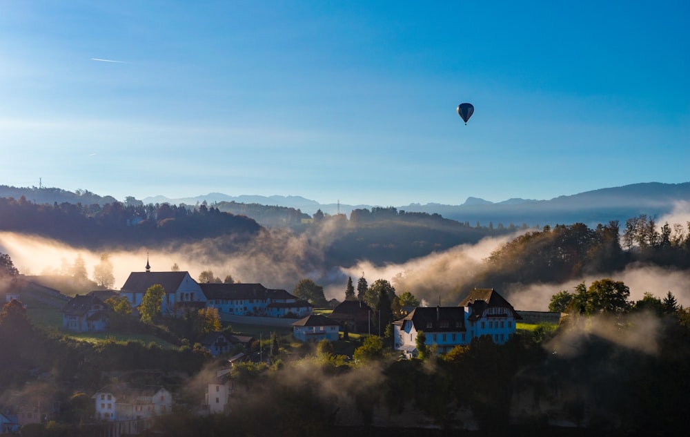 balão de ar quente voando sobre a montanha perto de casas sob o céu azul