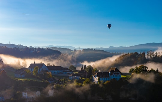 hot air balloon flying over mountain near houses under blue sky in Fribourg Switzerland