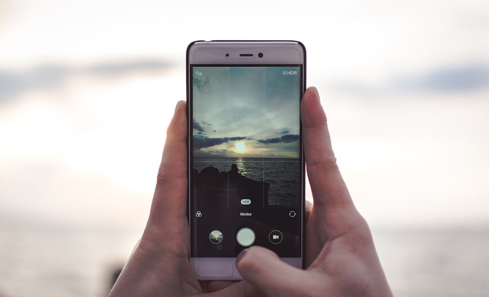 A person taking a picture of the ocean under clouds.