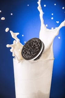 Artistic shot of a cookie being dipped into a glass of milk with soft red and white background tones.