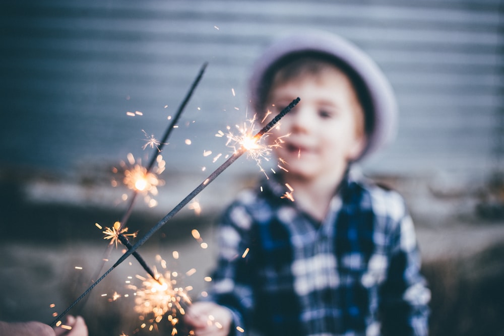 foto de closeup do menino vestindo camisa esportiva xadrez azul e branca segurando fogos de artifício