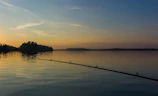 Wide-angle view of a serene Swedish lake at sunset with fishing rods lined up on the shore and a silhouette of a fisherman