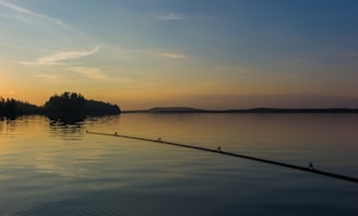 A calm lake with fishing rods resting on the shore at sunset.