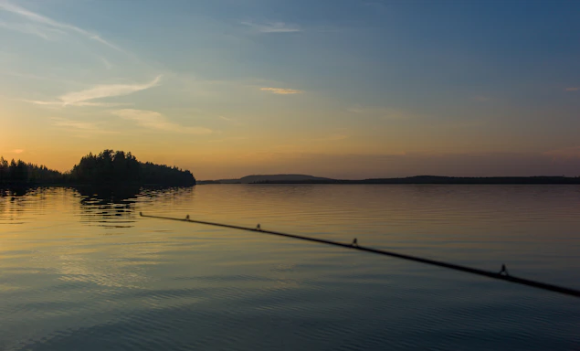 A cozy fishing spot by a calm lake at sunset with fishing gear laid out.