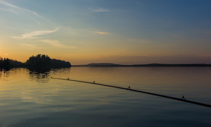 A serene southern lake at sunset with a small wooden dock and a fishing rod resting nearby.