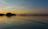 A serene lakeside scene at dusk with a fishing rod resting beside a tackle box filled with colorful lures.