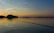 A serene lakeside scene at dusk with a fishing rod resting beside a tackle box filled with colorful lures.