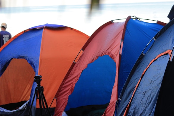 Several colorful camping tents are lined up, primarily in shades of blue and orange. A person in casual clothing is visible in the background.