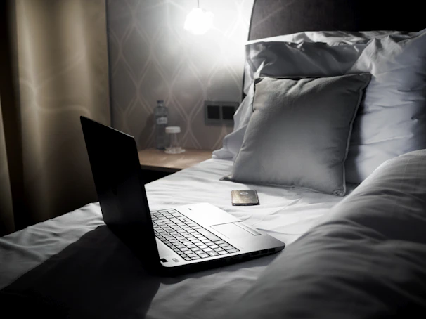 A sleek personal refrigerator sitting beside a cozy bedroom nightstand with a book and glass of water.