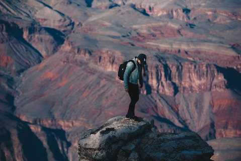 man standing on rock cliff overlooking canyon during daytime