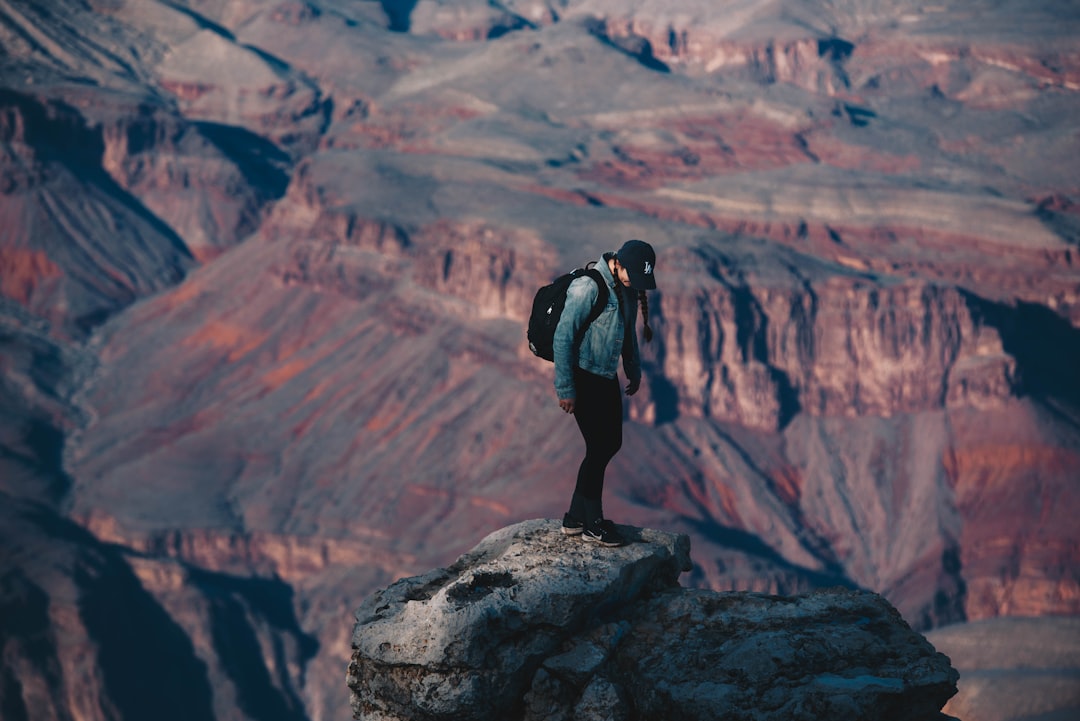 man standing on rock cliff overlooking canyon during daytime