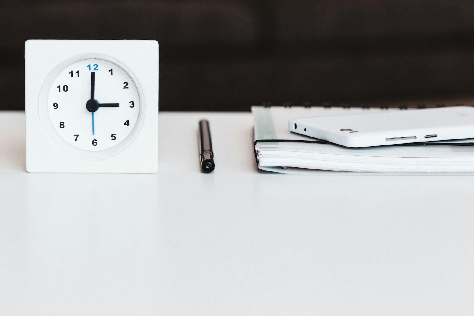 A desk clock beside a notebook and pen