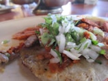 A close-up of a sizzling taco al pastor topped with fresh pineapple and cilantro on a rustic wooden table.