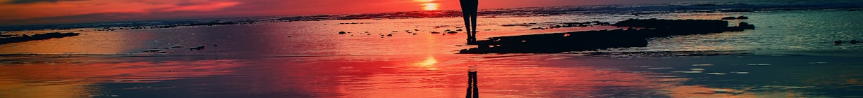 silhouette of person standing on rock surrounded by body of water