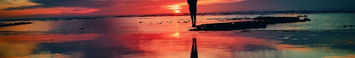 silhouette of person standing on rock surrounded by body of water