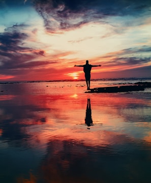 silhouette of person standing on rock surrounded by body of water