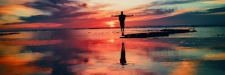 silhouette of person standing on rock surrounded by body of water