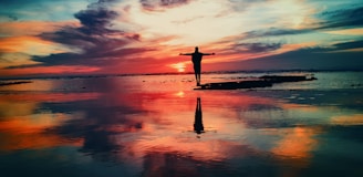 silhouette of person standing on rock surrounded by body of water