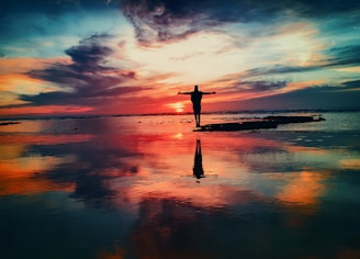 silhouette of person standing on rock surrounded by body of water