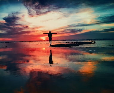 silhouette of person standing on rock surrounded by body of water